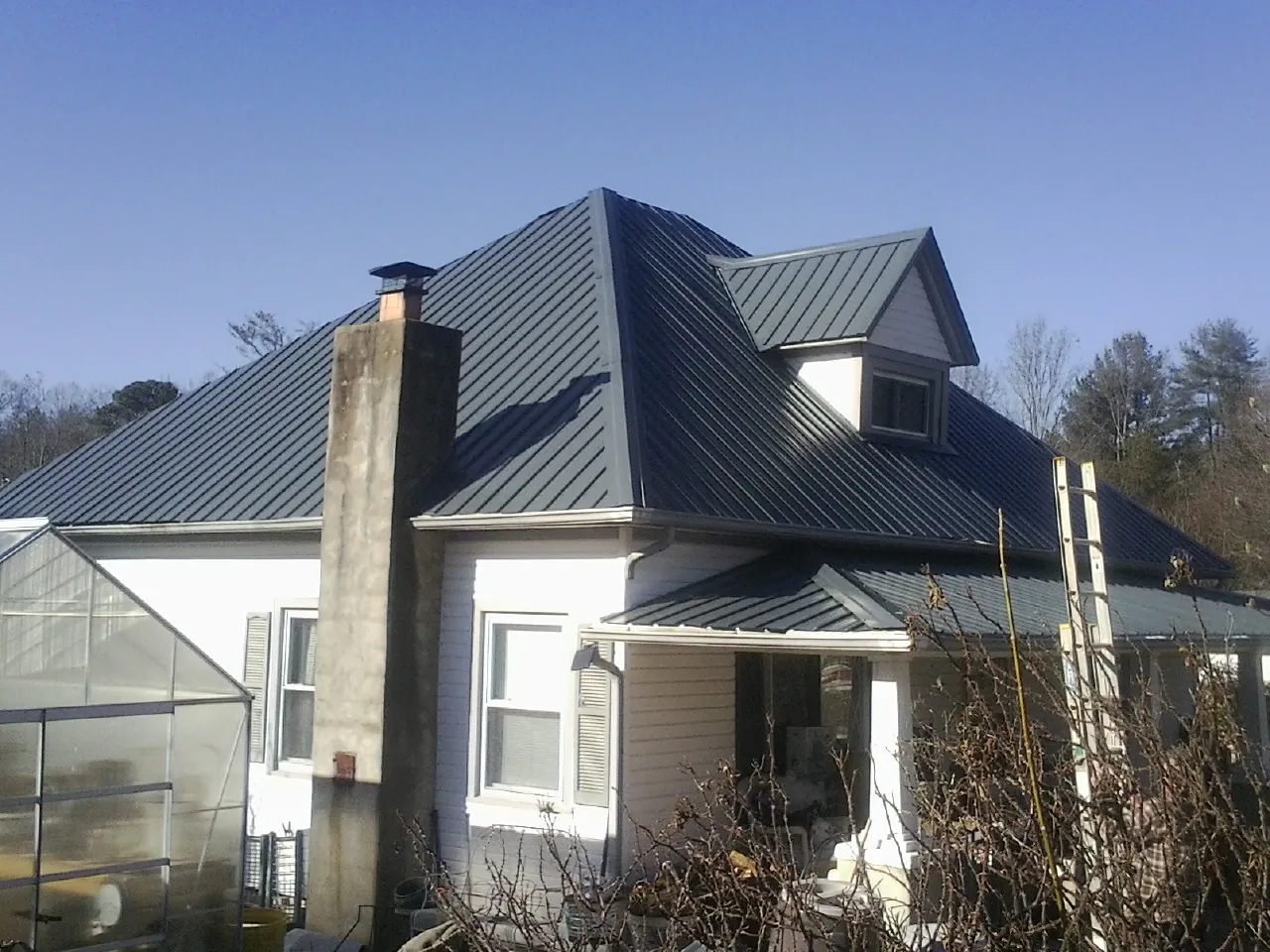 Dark blue standing seam metal roof on a white farmhouse with dormer — Slate & Tile Roof Repair by Roofing Brothers in Jourdanton