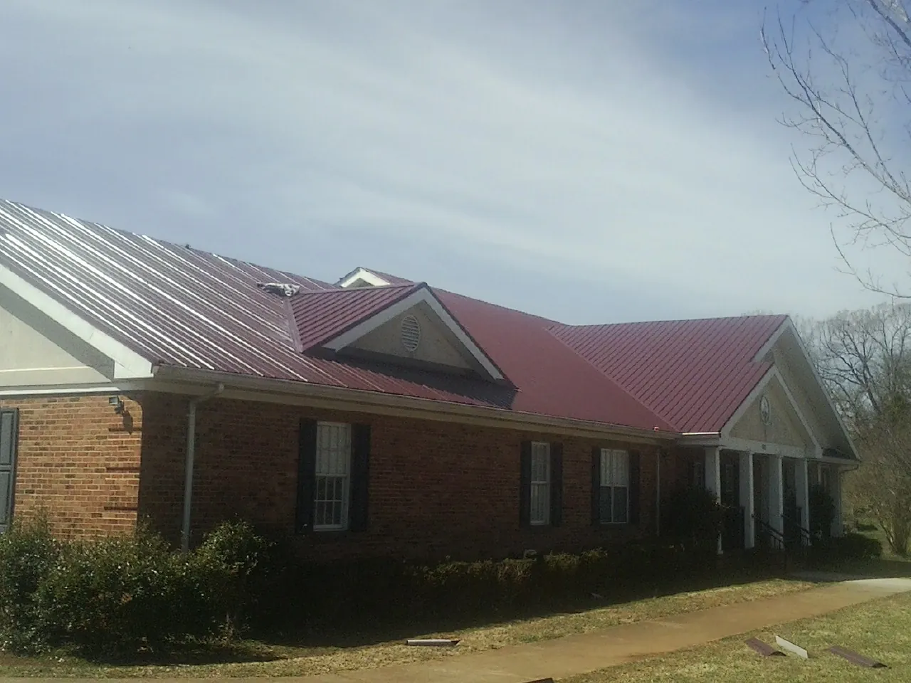 Red metal roof with gabled entries on a long brick building, from a Hail Damage Roof Repair job in Jourdanton
