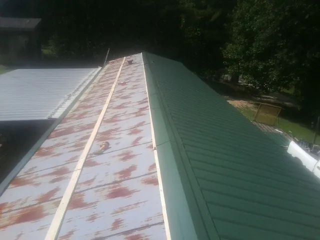 Old rusted panels beside newly installed green metal roofing — Wind Damage Roof Repair by Roofing Brothers in Jourdanton