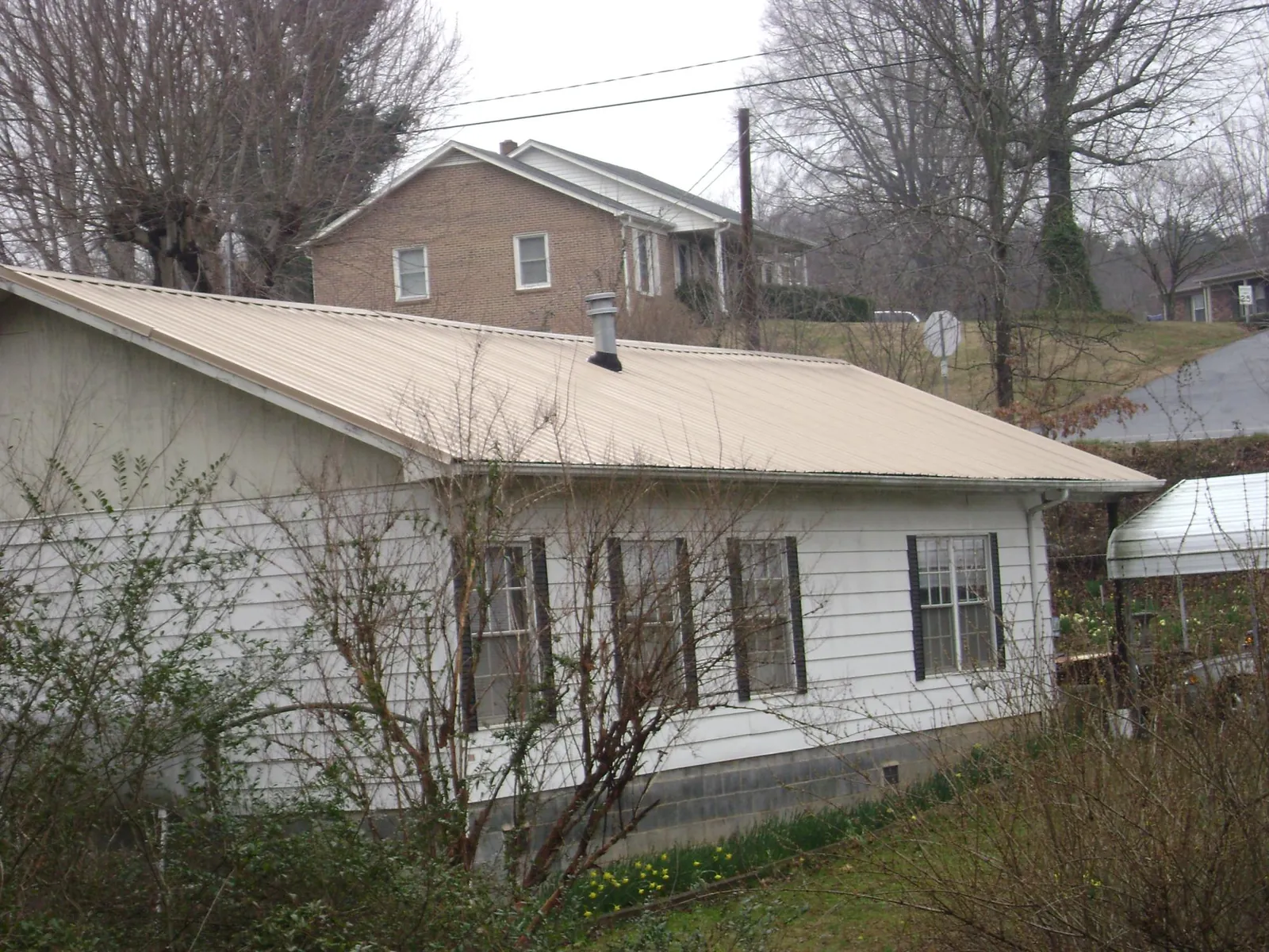 Tan metal roof on a white sided house set into a hillside — Commercial Roofing by Roofing Brothers in Jourdanton